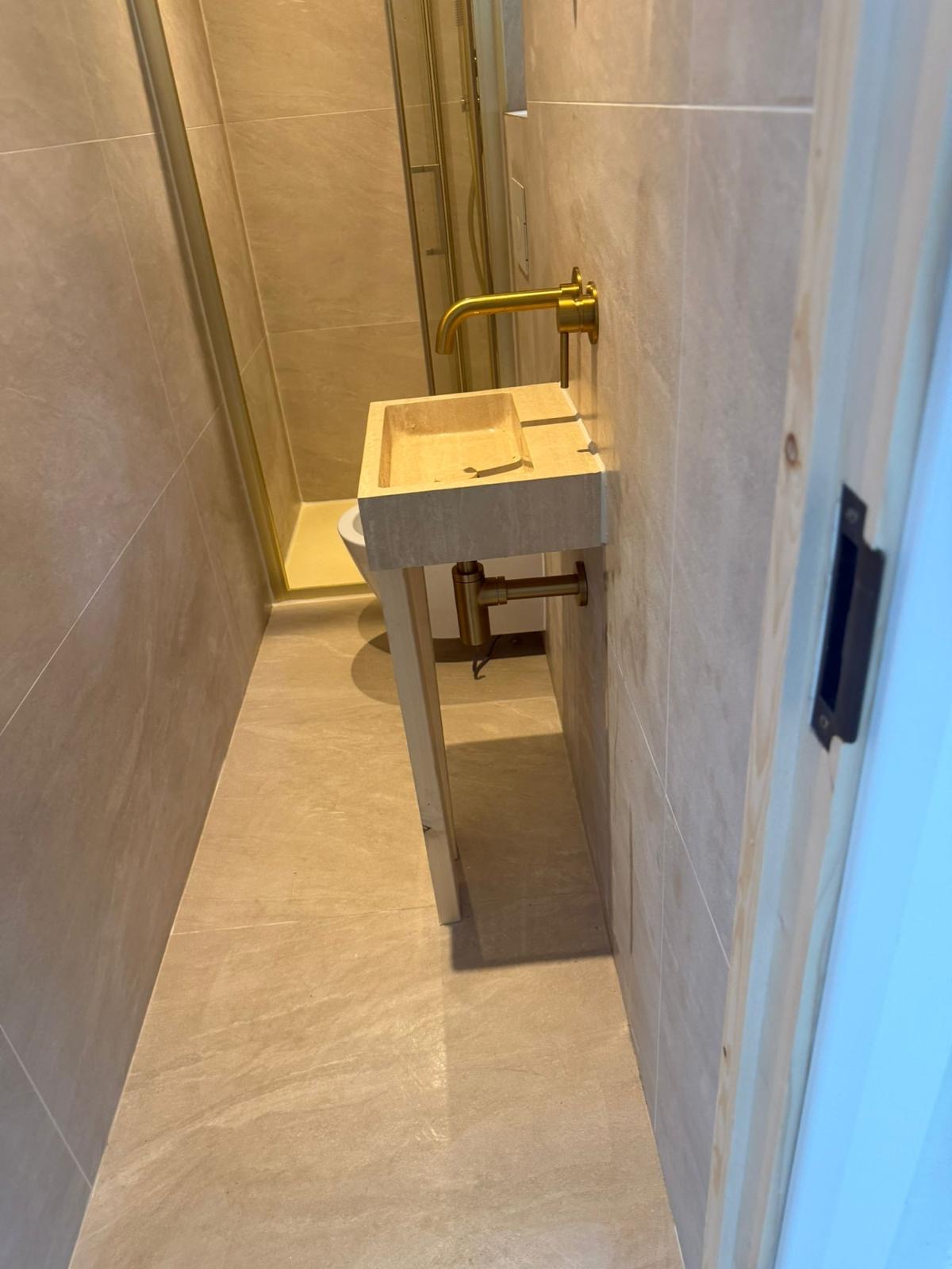 Compact cloakroom tiled walls and floor with wall mounted basin and brass tap